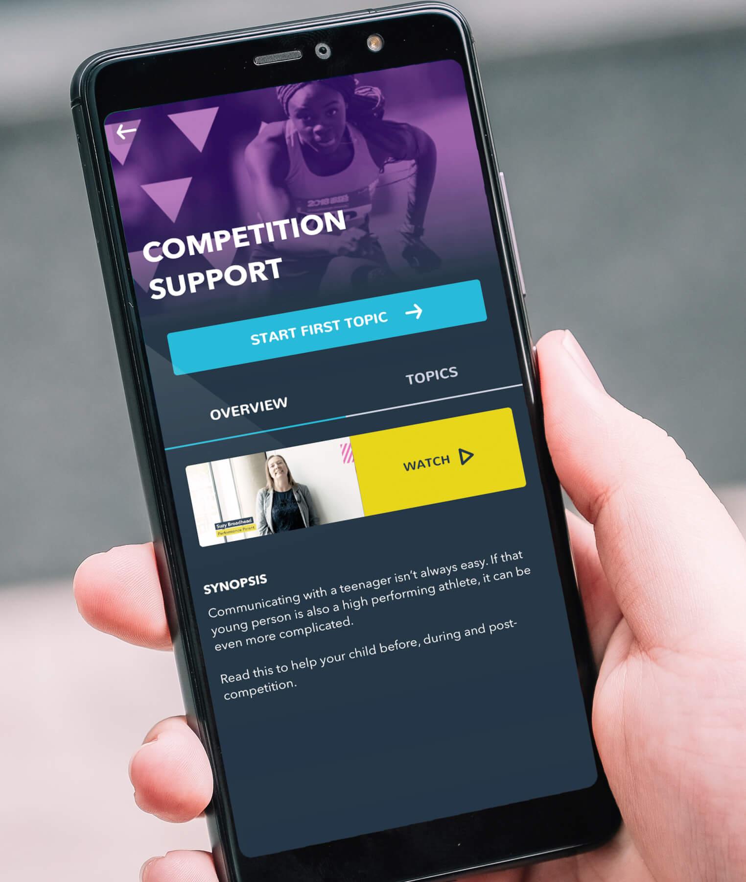A hand holds a smartphone displaying a support app with Competition Support at the top. The screen shows options to Start First Topic and Topics, plus a video section with Watch and a brief synopsis below.